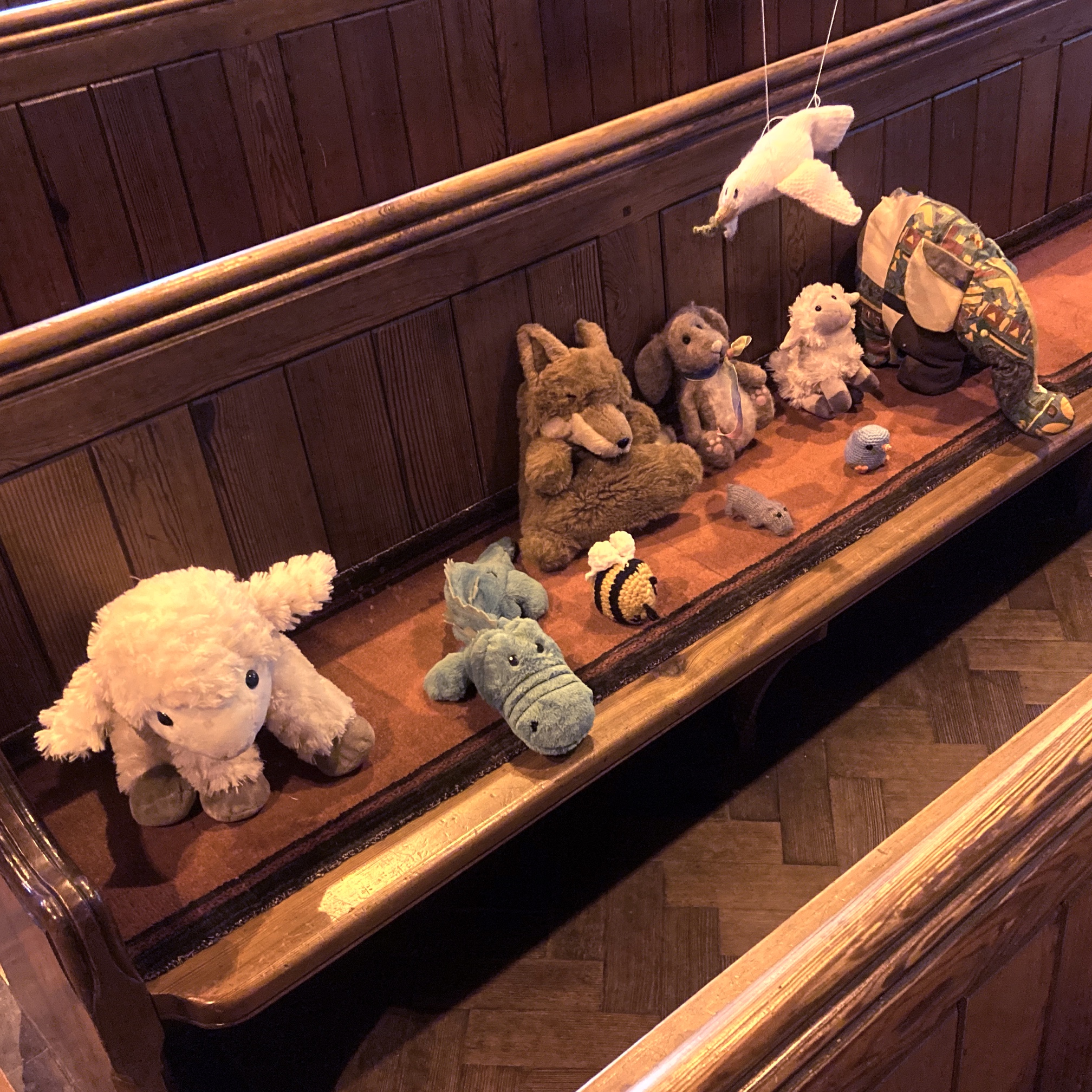 A row of cuddly animals on a pew.
