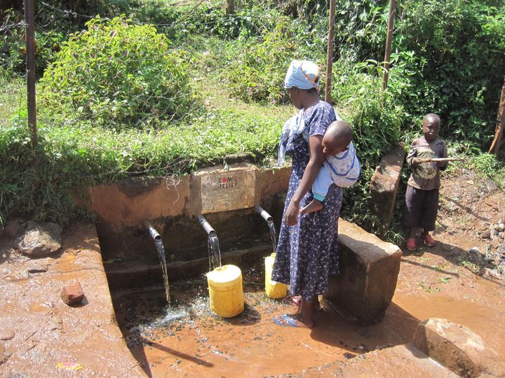 A woman collects water from a pipe.